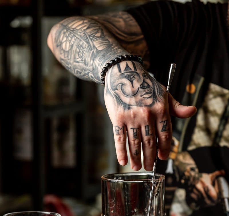Tatuaż na dłoni mężczyzny przedstawiający błazna bądź też klauna oraz litery tworzące znaczenie dla jego posiadacza