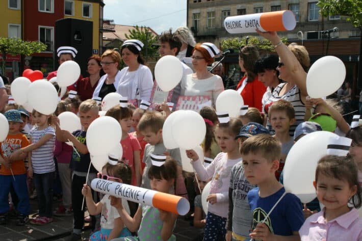dzieci z czerwono-białymi balonami i dużym papierosem promujące akcję społeczną