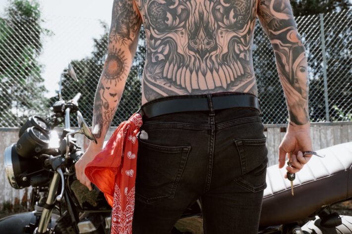 Osoba odwrócona tyłem prezentuje bogato zdobiony tatuaż na całych plecach oraz rękach, w tym symbol słońca na lewym przedramieniu