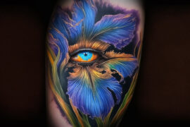 Zakrzywione płatki kwiatów w odcieniach niebieskiego i purpury otaczają realistycznie przedstawione ludzkie oko z błękitną tęczówką, które stanowi centralny punkt całego dzieła