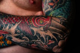 Tatuaż z intensywnymi czerwieniami i głębokimi czerniami obejmuje ramię, prezentując złożone, tradycyjne wzory i motywy