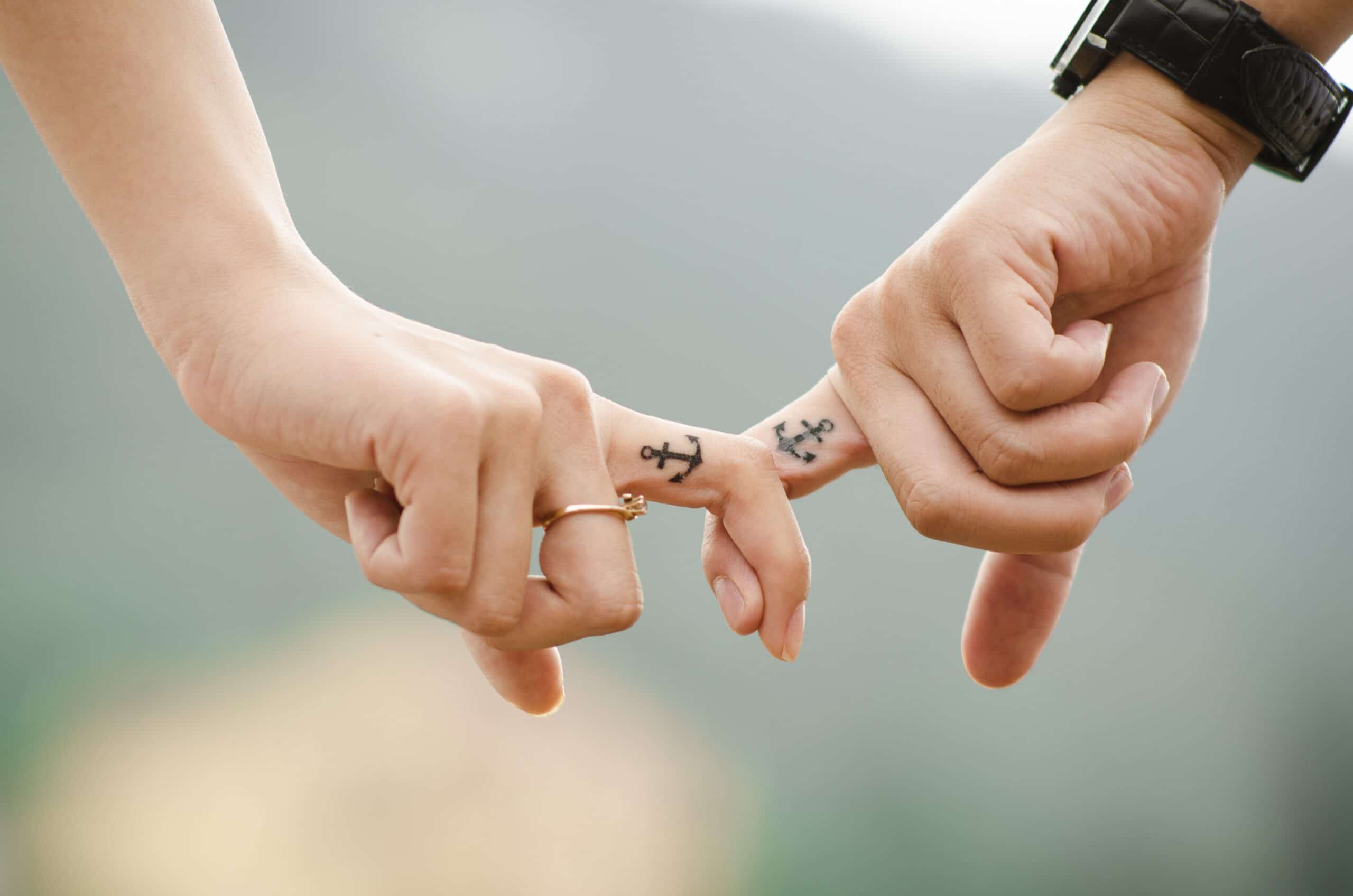 Tatuaz kotwica na palcach pary trzymającej się za dłonnie