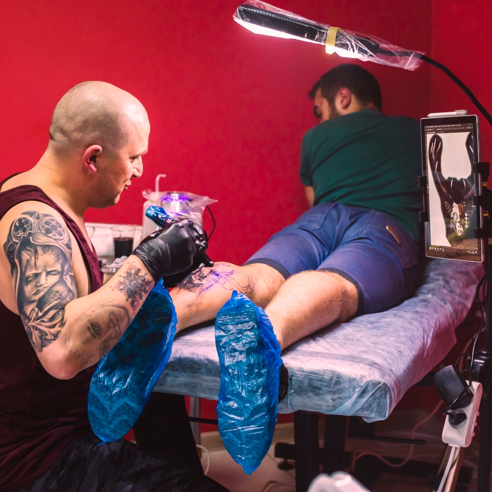 Studio tatuażu i mężczyzna robiącu drugiemy tatuaż na nodze