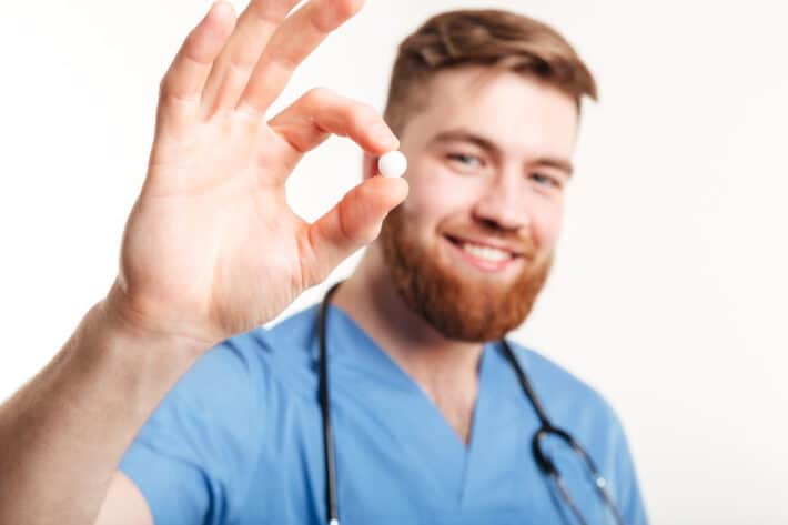 Mężczyzna który jest lekarzem tyrzyma w dłoni tabletke