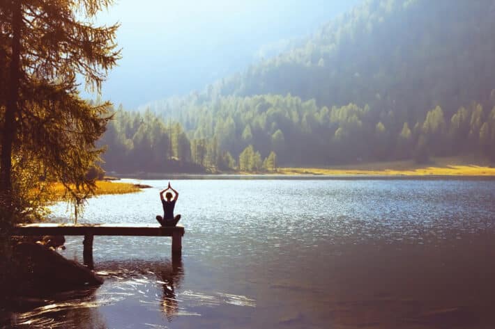 Kobieta uprawia joge na moście koło jeziora