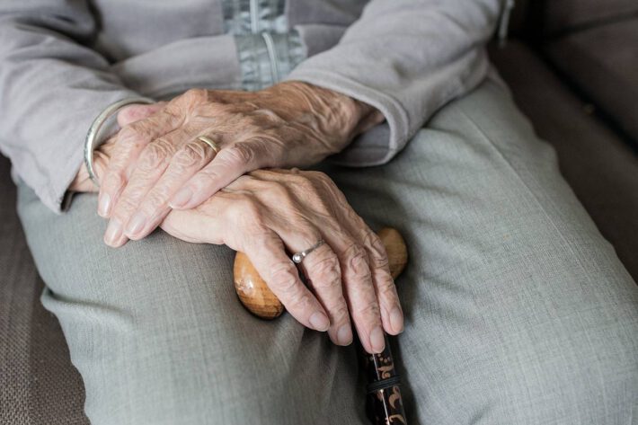 Starsza kobieta siedzi na krześle i trzyma w dłoni laskę