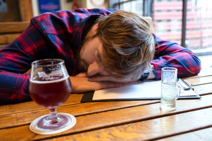 Mężczyzna uzależniony od alkoholu siedzi przy stoliku w barze