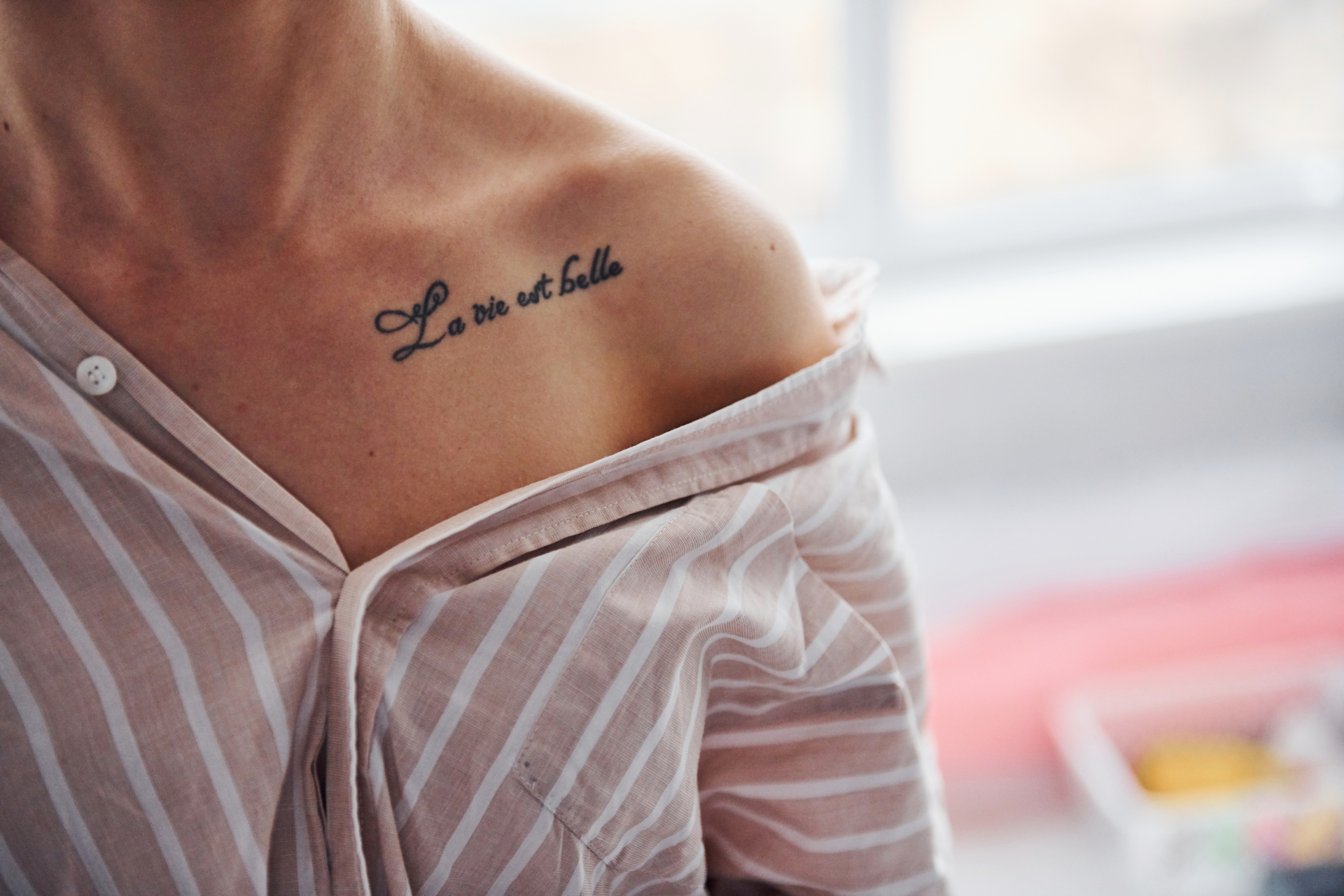 Kobieta ma na ramieniu tatuaż z napisem "La vie est belle", co oznacza "Życie jest piękne"