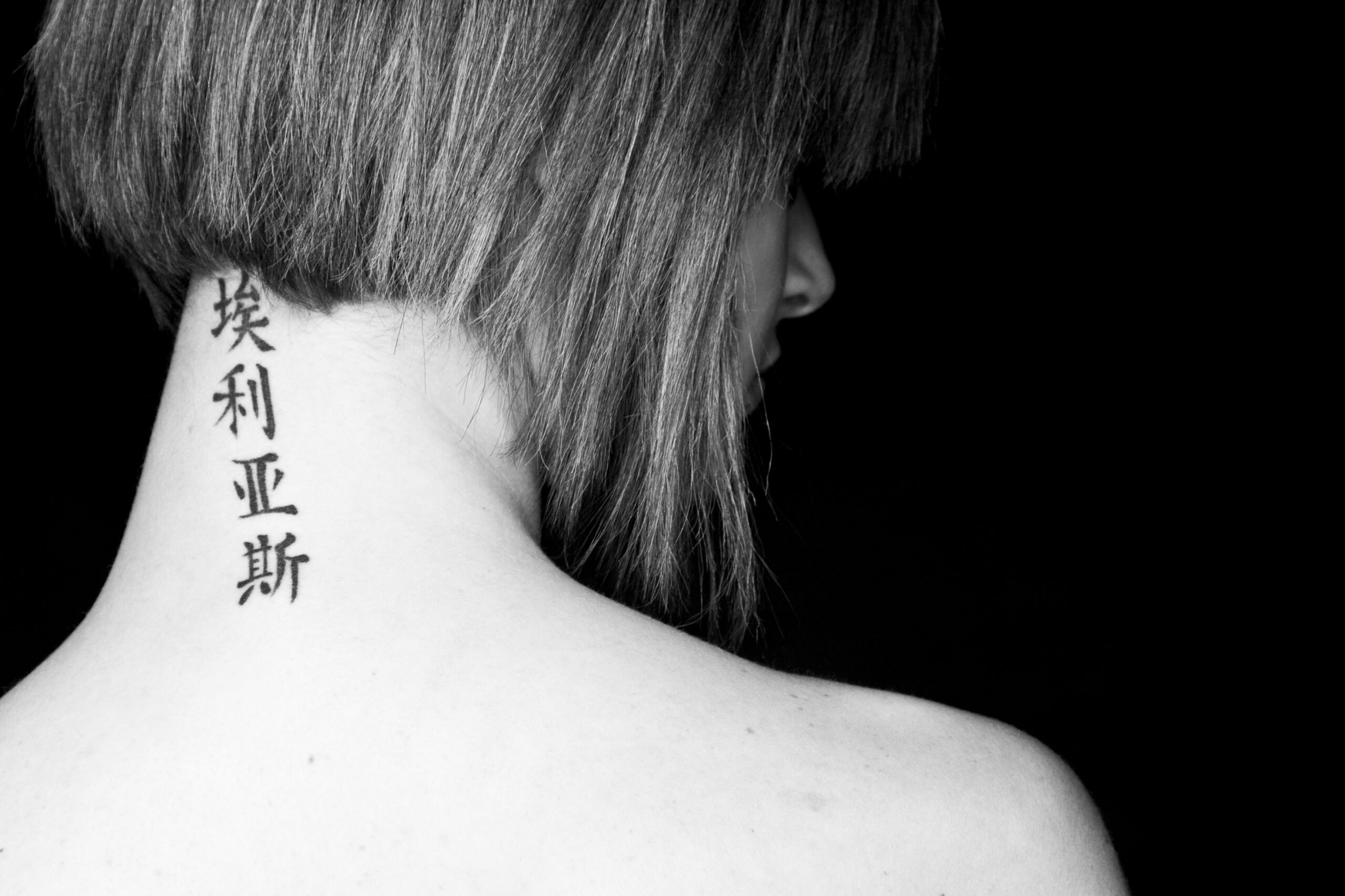 Mały tatuaż na szyi kobiety z tyłu przedstawiający napis po chińsku