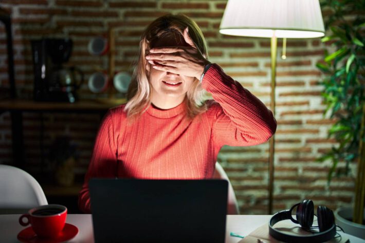 Kobieta pracująca przy komputerze zasłania swoje oczy dłonią