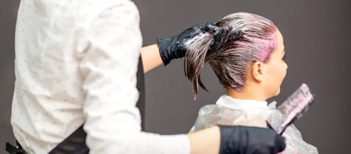 Na zdjęciu widać fryzjerkę w salonie fryzjerskim farbującą klientce włosy na różowy kolor.