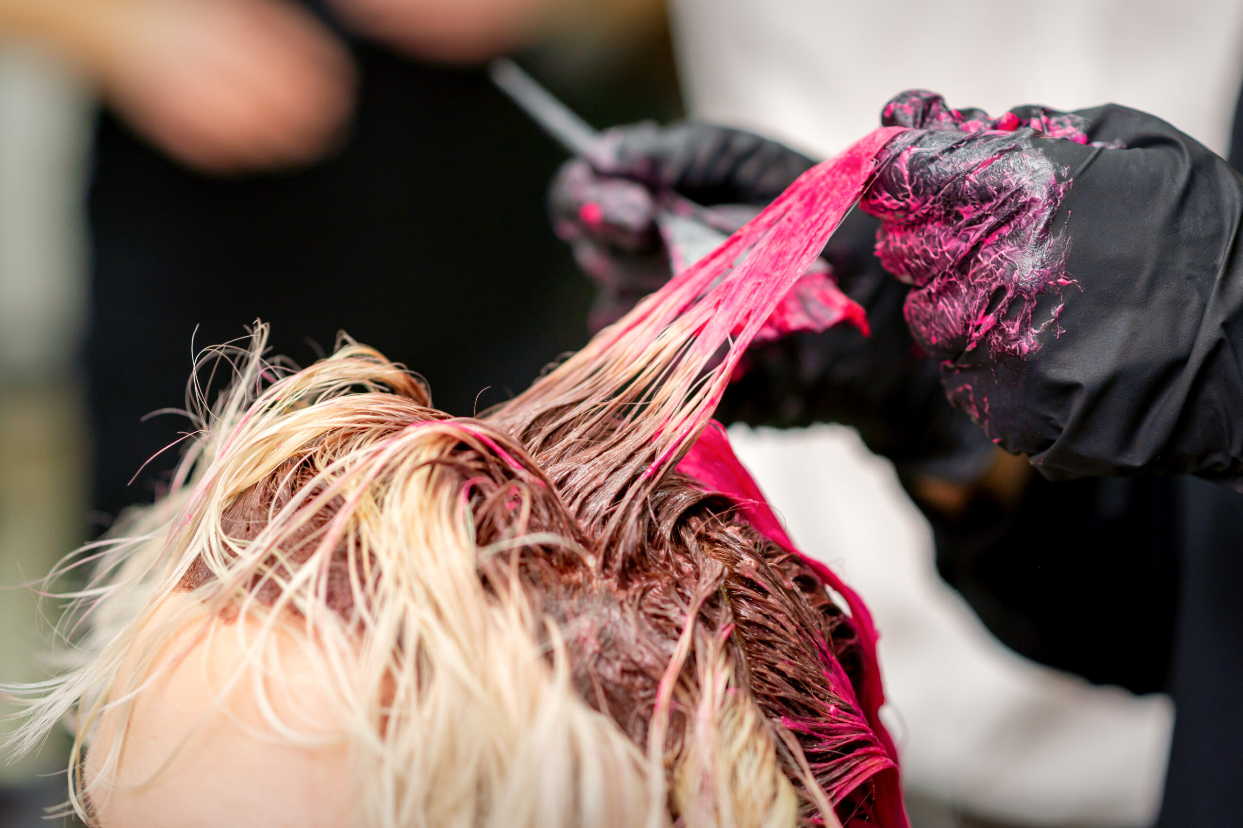 Przedstawiony na obrazku moment ukazuje kobietę siedzącą u fryzjera, podczas gdy stylistka precyzyjnie farbuje jej włosy od spodu. Ta odważna technika koloryzacji dodaje głębi i wyrazistości fryzurze, nadając kobiecie nowy, unikalny wygląd.