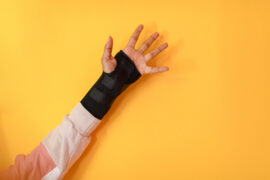 Stłuczona ręka dziecka w ortezie na tle żółtej ściany