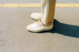 Zdjęcie przedstawia nogi mężczyzny w butach męskich na tle betonowej podłogi. Buty są klasyczne, czarne i wykonane ze skóry. Widać, że są to buty na sznurowanie, a ich cholewka sięga powyżej kostki. Mężczyzna stoi w pozycji neutralnej, co pozwala skupić uwagę na butach i ich wykonaniu. Obrazek ten ma na celu pokazanie, jak ważne jest odpowiednie obuwie w męskiej garderobie oraz jak klasyczne i eleganckie buty męskie mogą wpłynąć na cały wygląd mężczyzny.