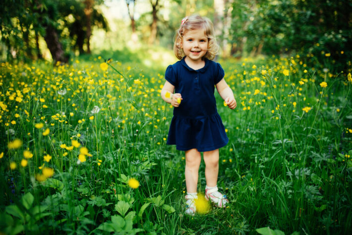 Na zdjęciu widoczna jest urocza dziewczynka, która stoi na zielonej trawie. Dziewczynka ma uśmiechniętą twarz oraz piękne, długie włosy opadające na ramiona. Na jej twarzy widać radość i beztroskę, a w tle widać piękne krajobrazy przyrody. Dziewczynka jest ubrana w kolorowe letnie ubrania, które podkreślają jej naturalne piękno i urok. Obrazek kojarzy się z beztroską, radością i pięknem natury, co może przyciągnąć uwagę osób zainteresowanych naturą, dziećmi oraz uroczymi imionami dla dziewczynek.