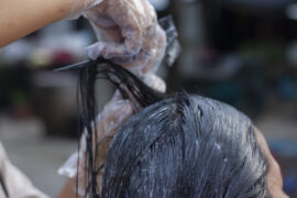 Na obrazku widać kobietę w salonie fryzjerskim, która farbuje włosy na ciemny kolor.