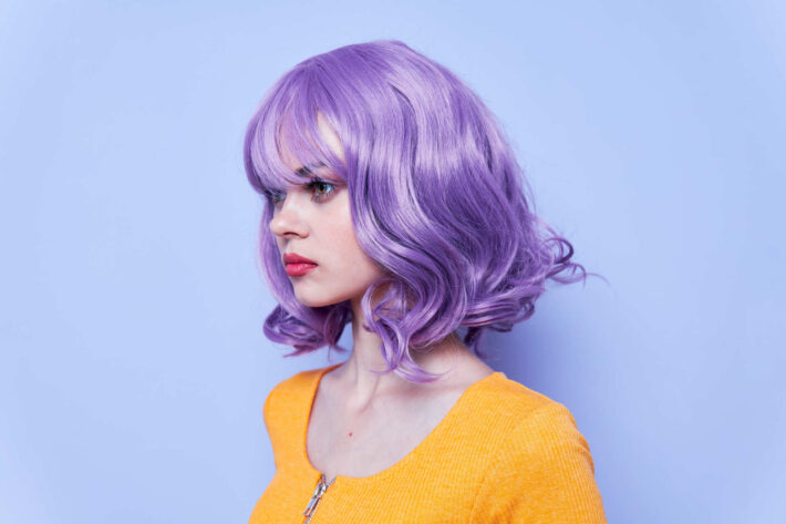 Kobieta z włosami zafarbowanymi gencjaną stojąca na fioletowym tle