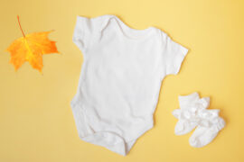 Na zdjęciu widać białe ubranko niemowlaka, które zostało właśnie wyprane i wygląda na czyste i pachnące. Ubranko znajduje się na jasnym żółtym tle, co nadaje zdjęciu przyjazny i ciepły klimat. Zdjęcie to może być użyte w artykule lub na stronie internetowej o praniu ubranek dziecięcych, aby zobrazować, jak ważne jest dbanie o higienę ubranek dla niemowląt i jakie mogą być najlepsze sposoby na pranie, aby utrzymać je w jak najlepszym stanie.
