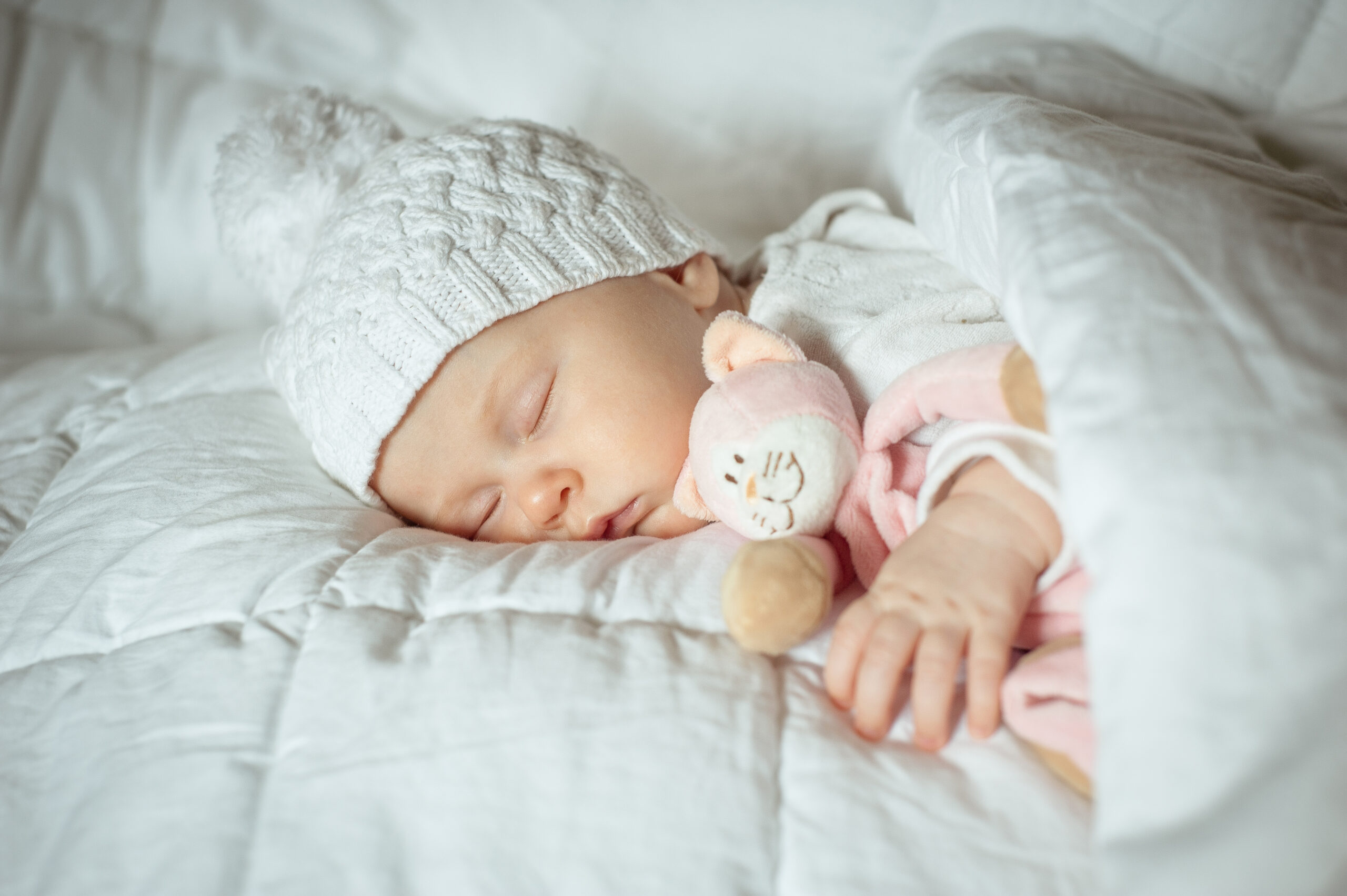 Na zdjęciu widoczny jest uroczy noworodek, ubrany w miękkie i przytulne ubranko oraz czapeczkę. Maluszek śpi spokojnie, z uśmiechem na twarzy, co może być dowodem na to, że jego ubranie jest wygodne i komfortowe. Taki obrazek może przypominać każdemu, jak ważne jest, aby wybierać odpowiednie ubrania dla noworodka, które zapewnią mu wygodę i bezpieczeństwo już od pierwszych chwil życia.