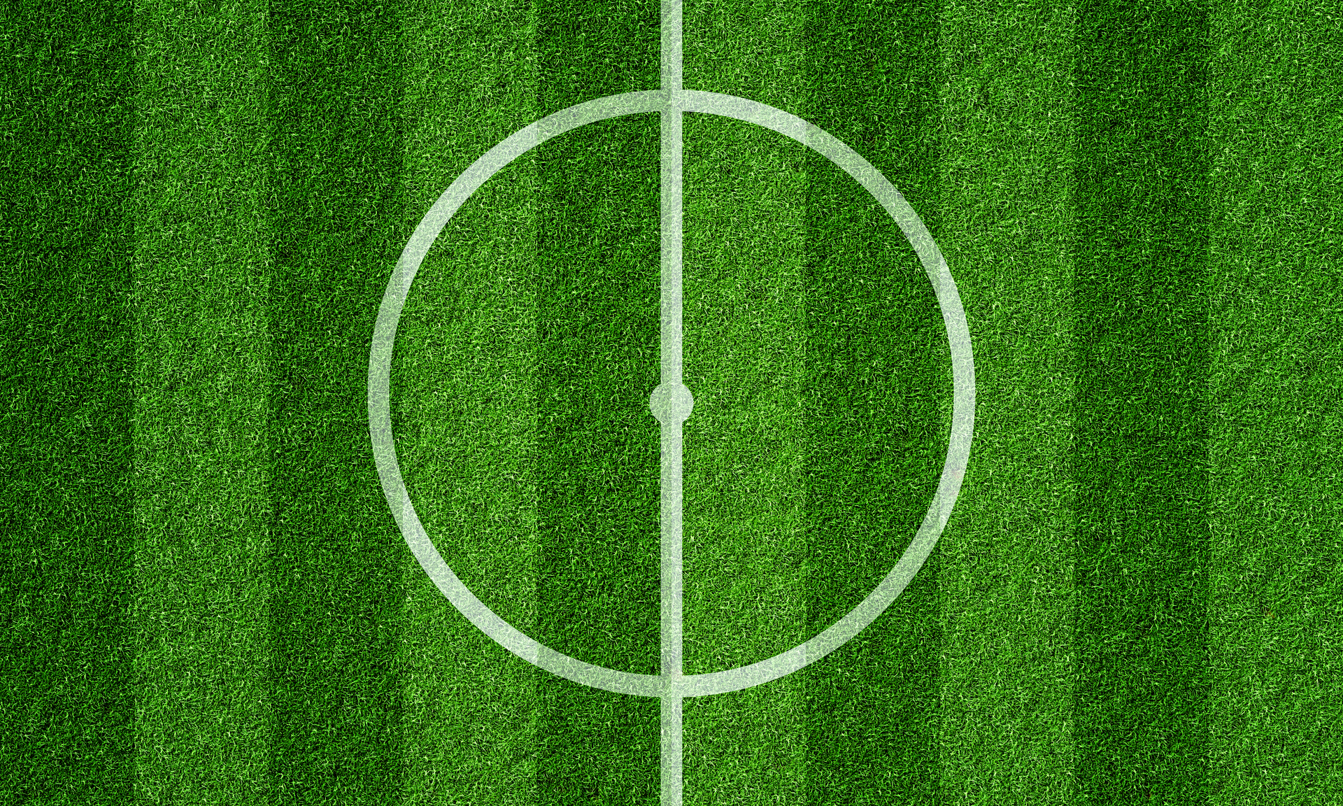 Ten wyrazisty obrazek przedstawia białe koło umieszczone centralnie na boisku piłkarskim. Koło wydaje się być punktem centralnym i wyróżnia się na tle trawy o żywym odcieniu zieleni. Obrazek ukazuje precyzję i symetrię, podkreślając znaczenie tego elementu na boisku oraz sugerując, że jest to część istotnej struktury gry w piłkę nożną