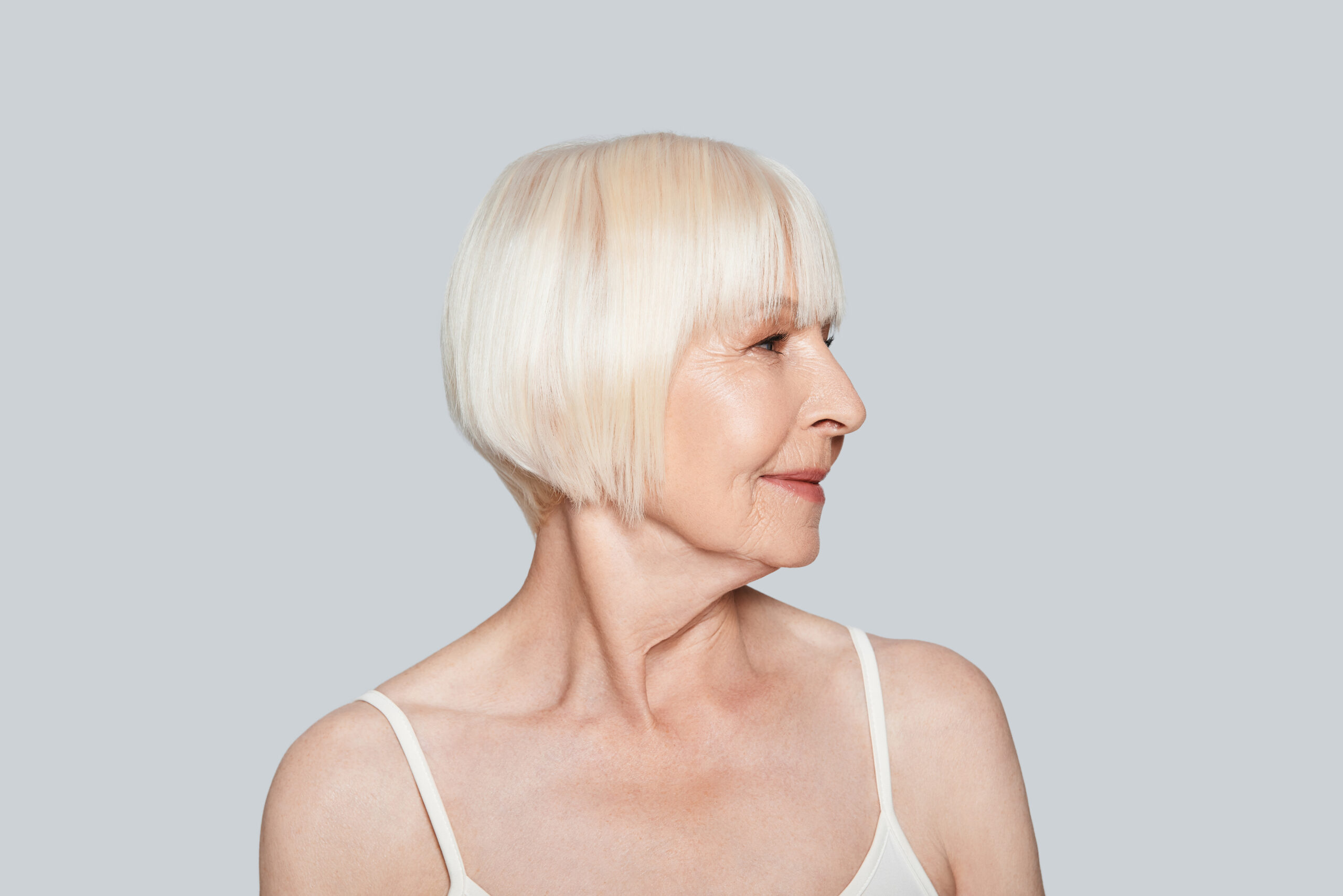 Przedstawione zdjęcie ukazuje kobietę w wieku 50 lat, która ma na sobie krótką fryzurę o mdłym kolorze. Włosy kobiety są zaczesane na bok i lekko ułożone, co nadaje jej delikatnego wyglądu. Kobieta patrzy w kamerę z uśmiechem, co może sugerować, że czuje się komfortowo w swojej fryzurze