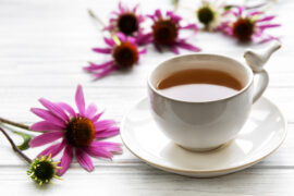 Obrazek ukazuje wyjątkową scenerię z filiżanką aromatycznej herbaty z jeżówki, której barwa emanuje ciepłem i przyjemnością. Wokół niej unoszą się delikatne liście jeżówki, dodając kompozycji naturalnego piękna. Ta mistyczna herbata zaprasza do chwili relaksu, przynosząc nie tylko niezwykłe smaki, ale także korzyści zdrowotne związane z jeżówką pospolitą