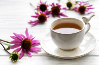 Obrazek ukazuje wyjątkową scenerię z filiżanką aromatycznej herbaty z jeżówki, której barwa emanuje ciepłem i przyjemnością. Wokół niej unoszą się delikatne liście jeżówki, dodając kompozycji naturalnego piękna. Ta mistyczna herbata zaprasza do chwili relaksu, przynosząc nie tylko niezwykłe smaki, ale także korzyści zdrowotne związane z jeżówką pospolitą