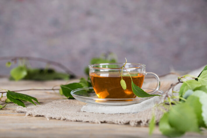 Na tym obrazku możemy zobaczyć filiżankę pełną aromatycznej herbaty z liści orzecha włoskiego, która zachwyca głębokim brązowym kolorem i intensywnym zapachem. Liście orzecha włoskiego unoszące się na powierzchni napoju dodają mu naturalnego uroku i świeżości. Ta wyjątkowa herbata nie tylko doskonale smakuje, ale również posiada liczne właściwości zdrowotne, wspierając nasze zdrowie i dobre samopoczucie dzięki swojemu bogactwu składników odżywczych i antyoksydantów