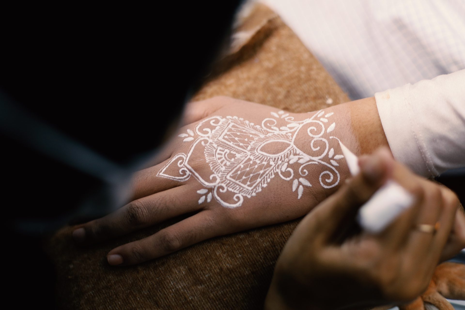 Na tym obrazku możemy zobaczyć proces tworzenia białego tatuażu na dłoni. Wprawne ręce tatuażysty delikatnie nanoszą biały tusz na skórę, tworząc precyzyjne linie i wzory. Cały proces jest pełen precyzji i skupienia, co podkreśla profesjonalizm i artystyczną wrażliwość wykonawcy