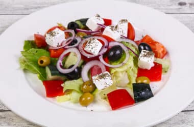 Świeża i kolorowa sałatka grecka podana na eleganckim białym talerzu. Soczyste pomidory, chrupiący ogórek, oliwki i ser feta tworzą apetyczną kompozycję. Tradycyjny smak Grecji w każdym kęsie, idealna przekąska na letnie dni
