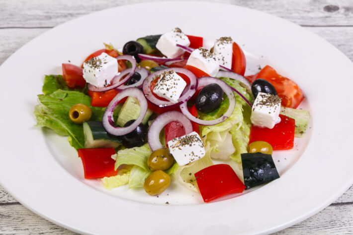 Świeża i kolorowa sałatka grecka podana na eleganckim białym talerzu. Soczyste pomidory, chrupiący ogórek, oliwki i ser feta tworzą apetyczną kompozycję. Tradycyjny smak Grecji w każdym kęsie, idealna przekąska na letnie dni