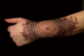 Tatuaż mandala znajdujący się na przegubie dłoni ukazanej na czarnym tle